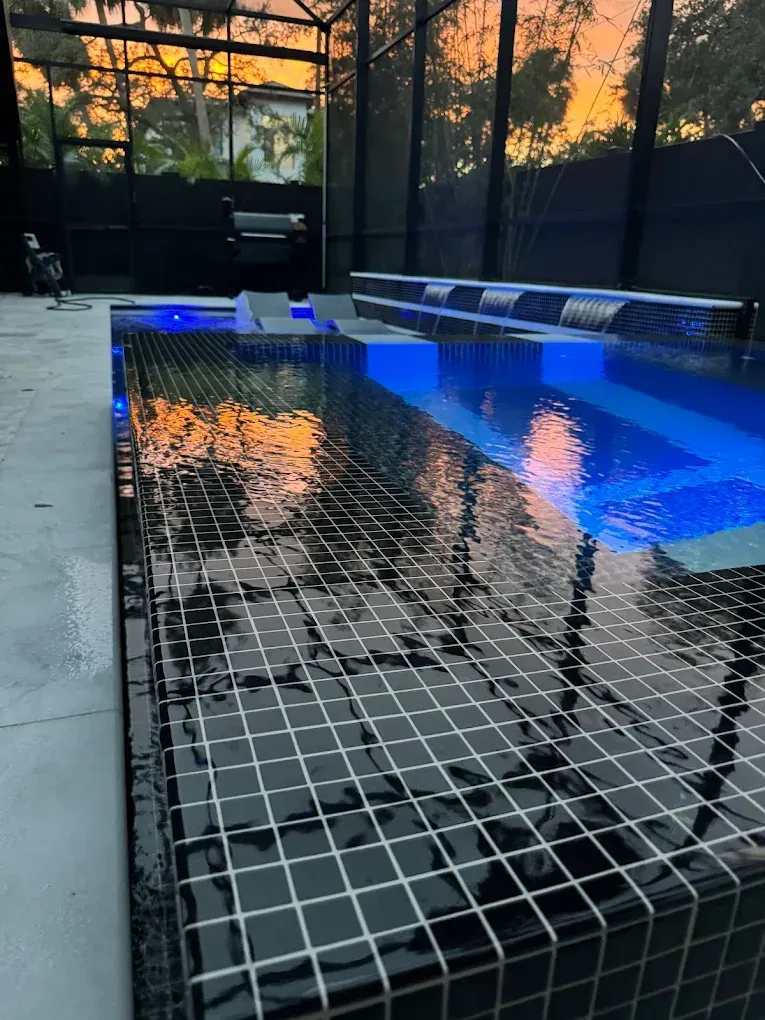 Modern pool with black tile, water, and blue lighting reflecting an orange sunset.