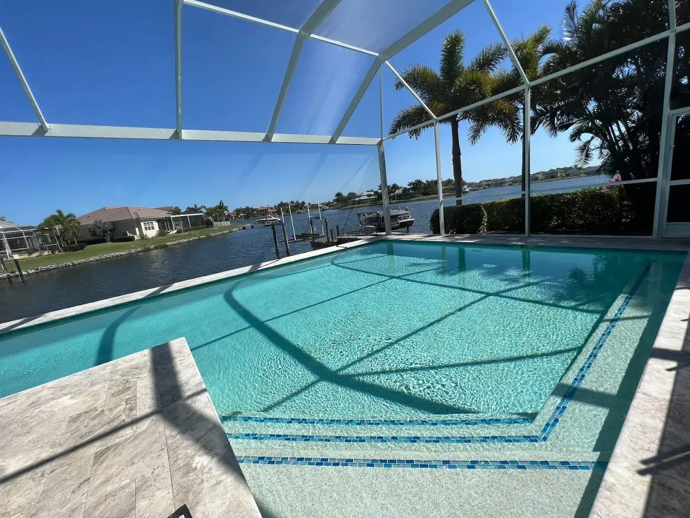 Pool with clear water, blue tile accents, surrounded by a screened enclosure overlooking a canal.