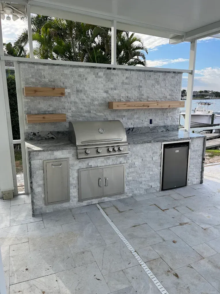 Outdoor kitchen with a grill, refrigerator, stone facade, and wooden shelves.