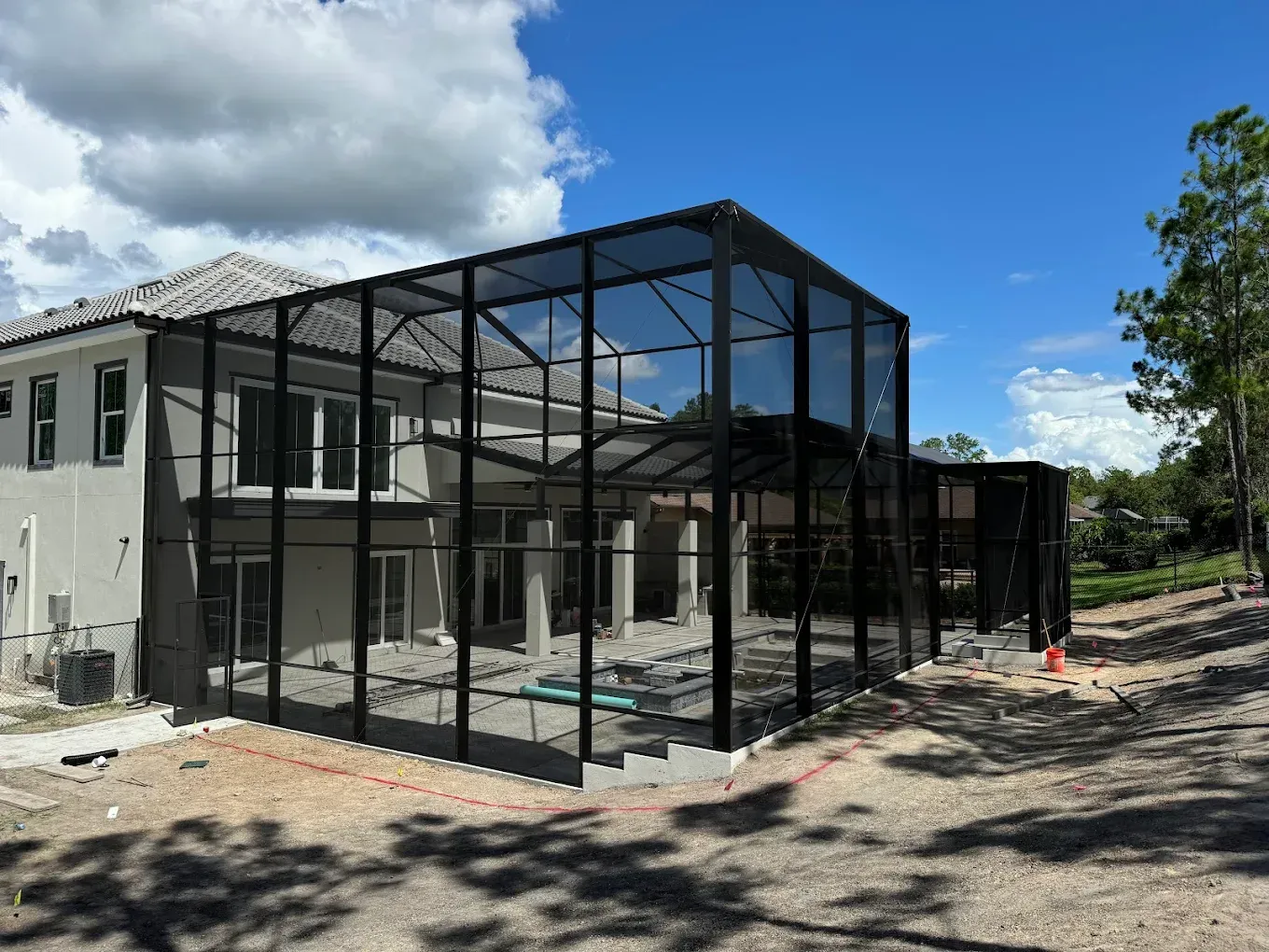 Black screened pool enclosure attached to a light-colored house under a partly cloudy sky.
