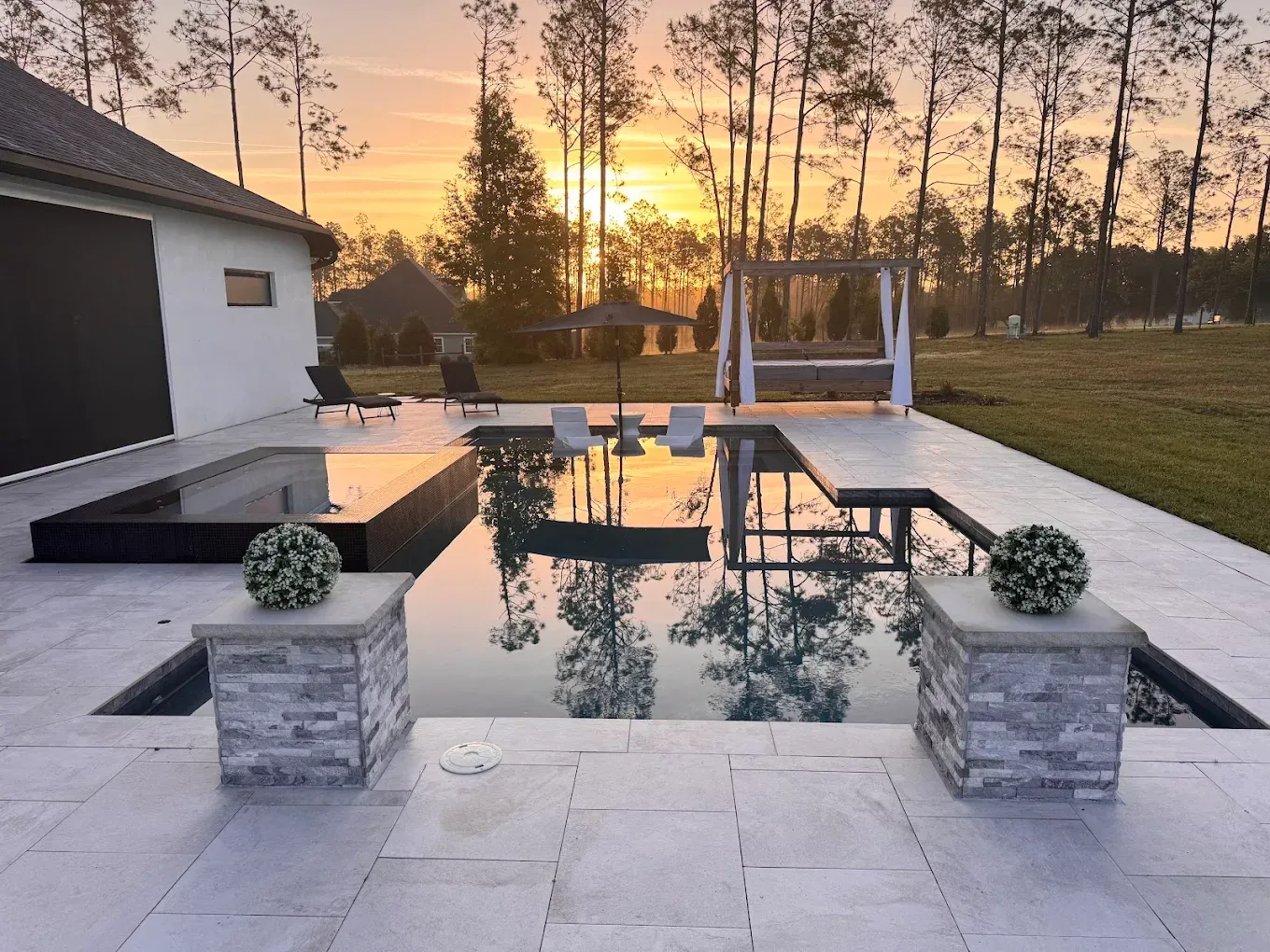 Poolside scene at sunset; pool with reflective water, stone patio, and hanging bed.