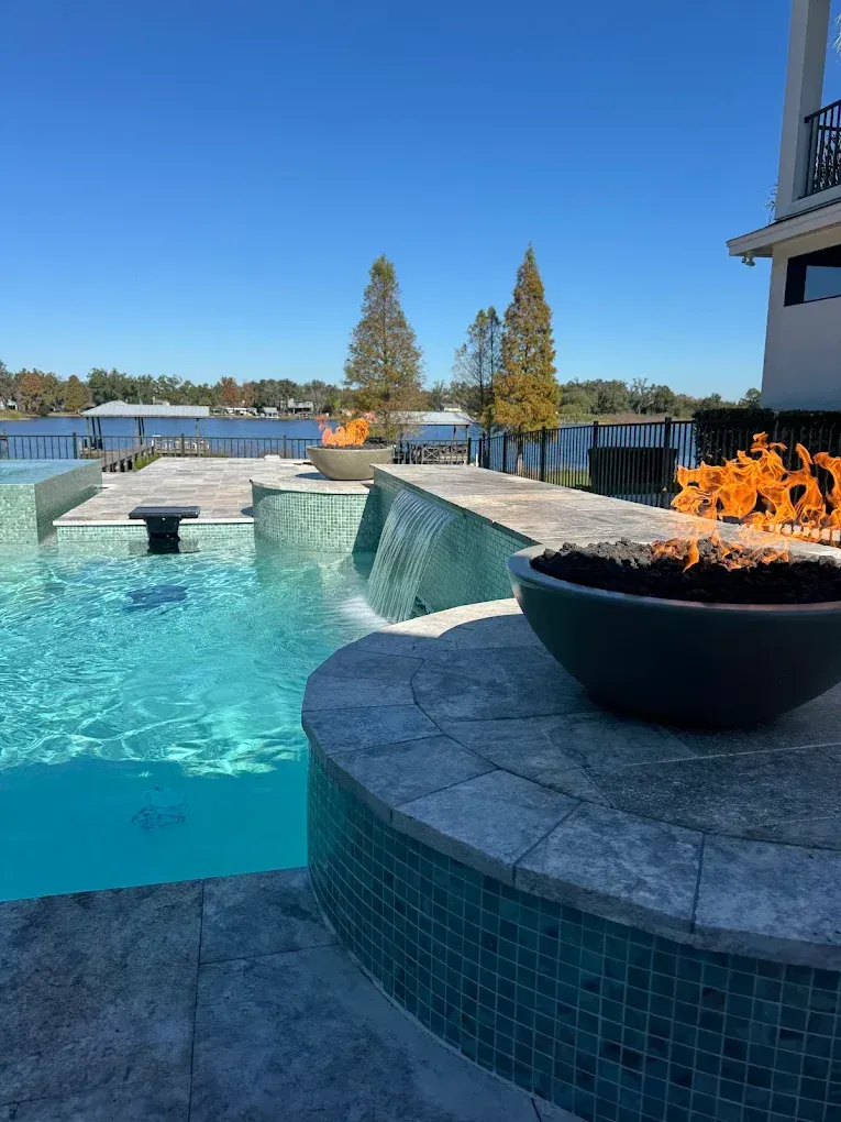 Poolside with fire bowl feature, waterfalls, blue water, and clear sky.