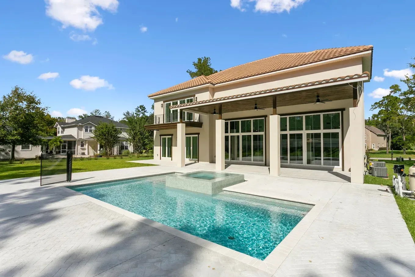 Luxury home exterior with pool. Beige stucco, terracotta roof, glass doors, and blue water.