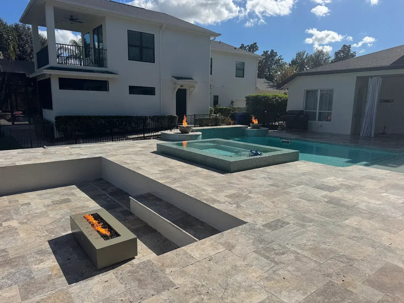 Backyard with pool, hot tub, and fire features. White house in background.