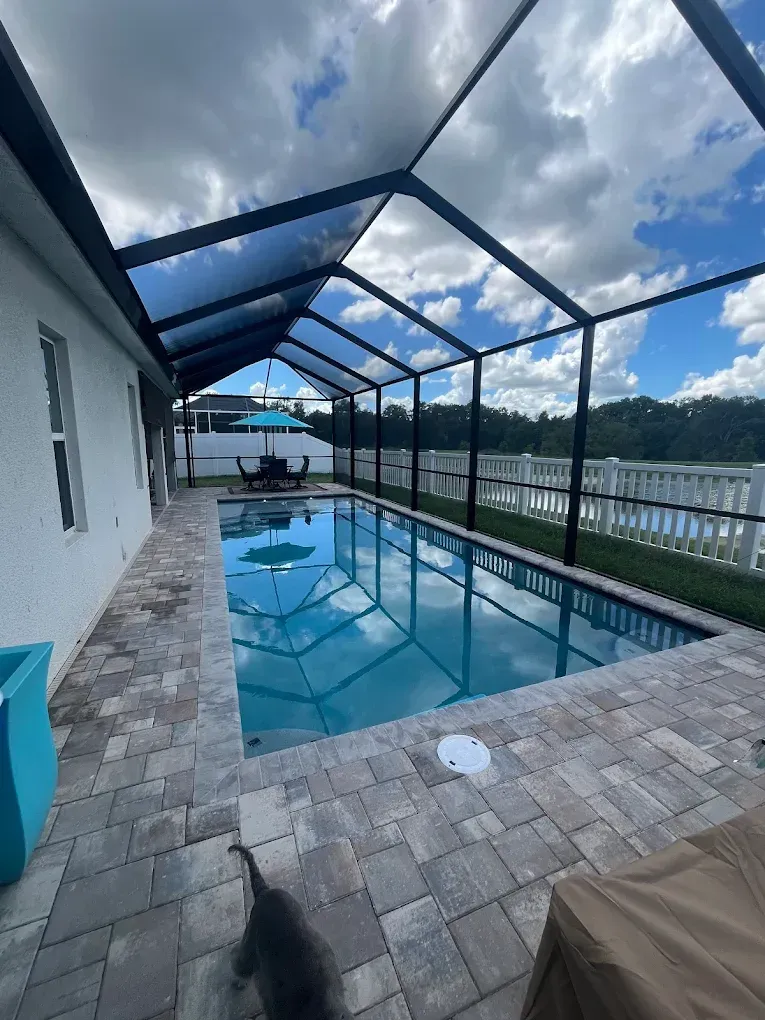Pool enclosed in a screen with blue water, surrounded by brick patio. Reflecting sky.