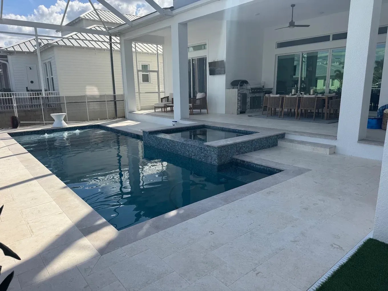 Pool and spa area with white patio and house, enclosed with screen.