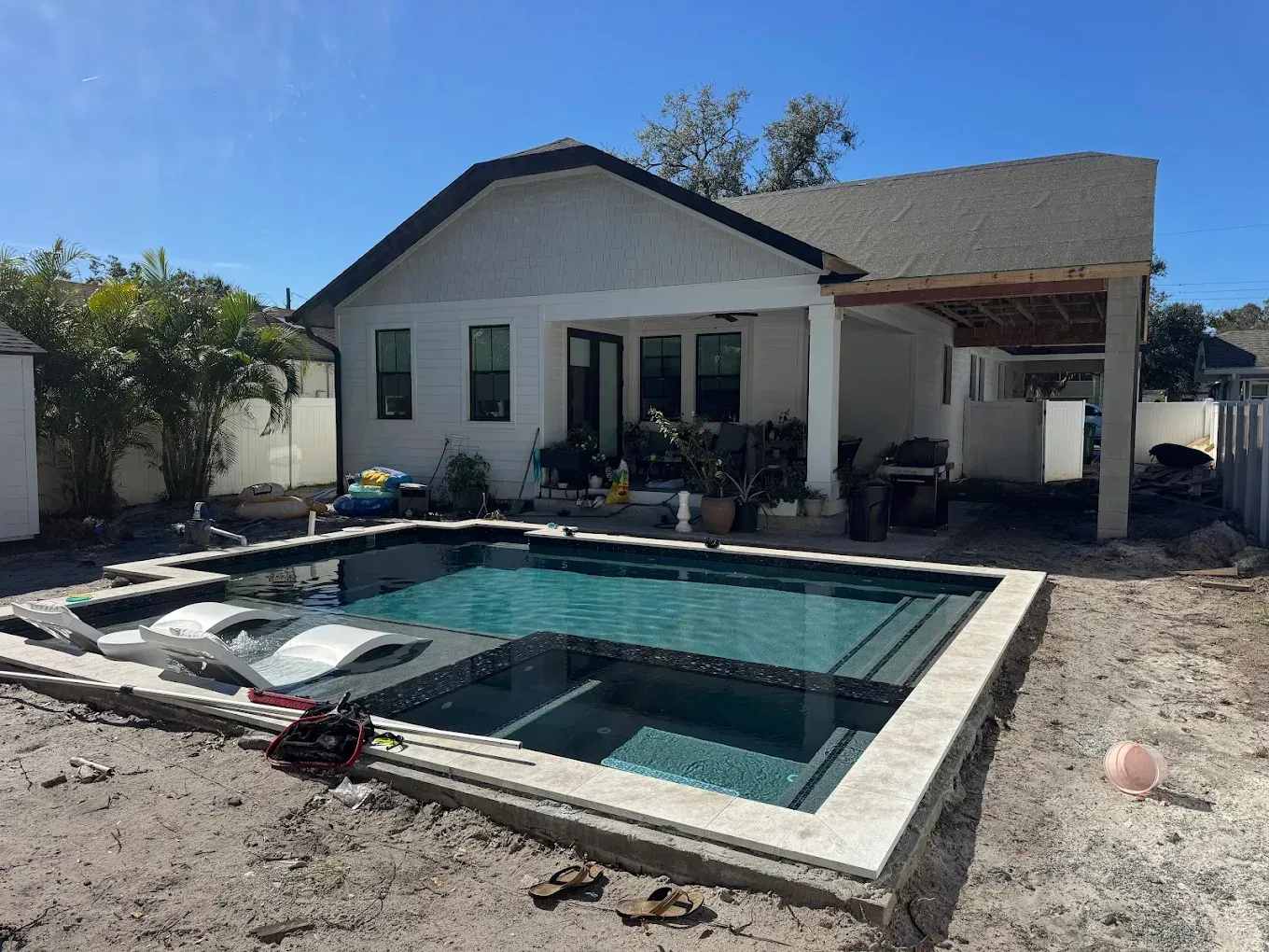 Backyard pool under construction, next to a white house with a covered patio.