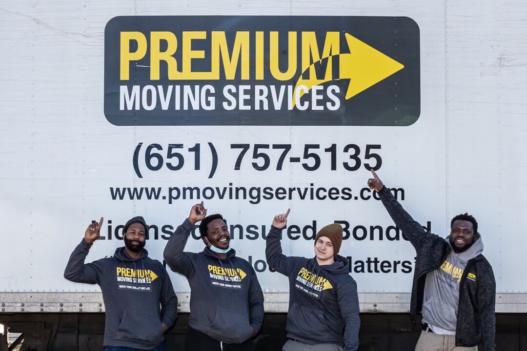 Four professional movers standing on the side of Premium Moving Services box truck after loading for a long distance move.