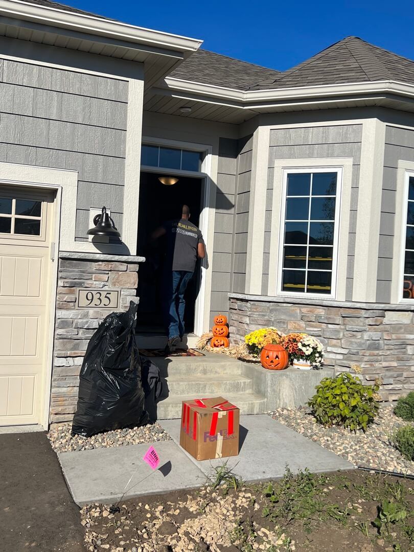 Mover unloading moving boxes into new house in Newport, MN through front door with halloween pumpkin decorations on front porch.