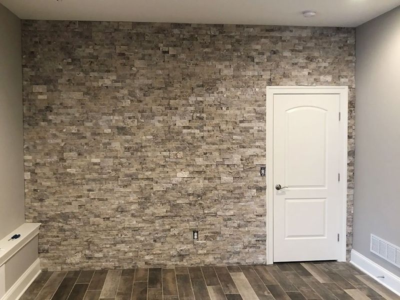 Stone accent wall with white door and hardwood floor. Beige and gray color scheme.