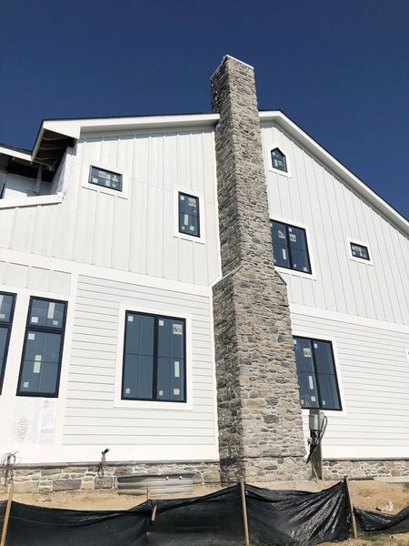 White house with a stone chimney and dark-framed windows against a clear blue sky.