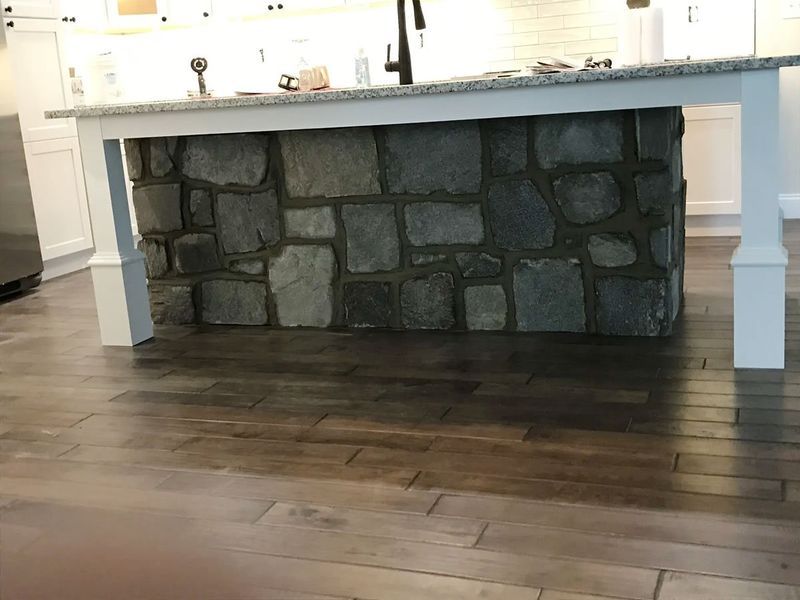 Kitchen island with stone base, granite countertop, white pillars, and wood flooring.