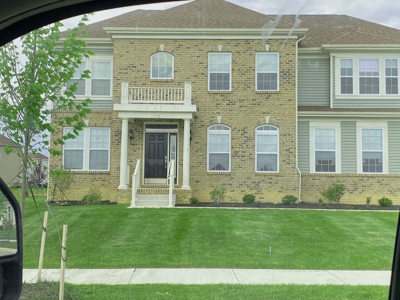 Two-story house with tan brick and green siding. Well-manicured lawn and white window frames.