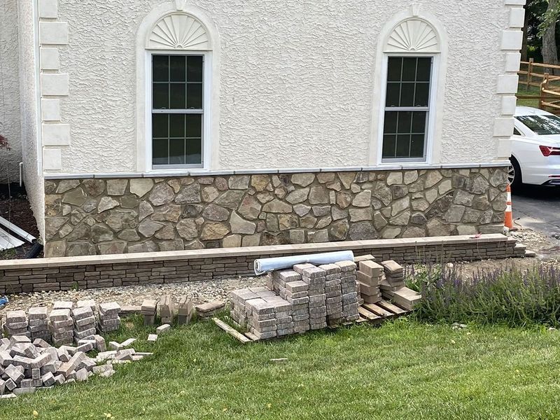 Stone veneer on house exterior, construction in progress; blocks and supplies on grass.