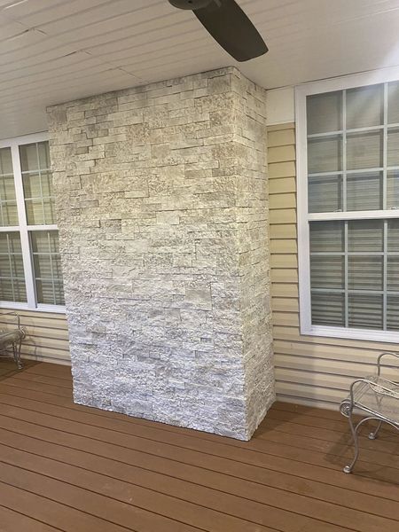 Brick-faced pillar on a deck between two windows, under a porch roof. Brown deck, tan siding, and a ceiling fan are visible.