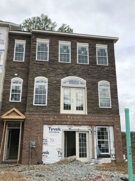 Three-story townhouse exterior with brick and stone facade, windows, and unfinished construction.