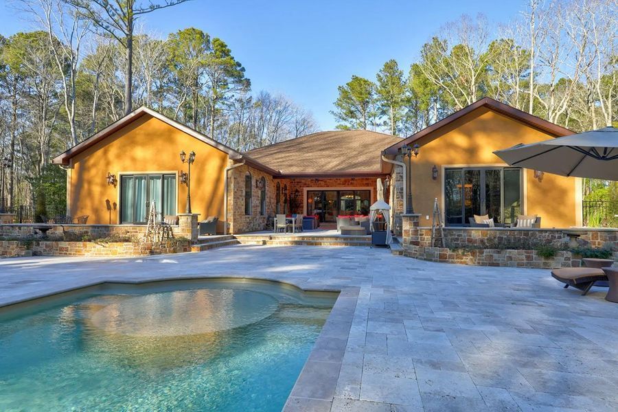 Backyard with pool, patio, and house with stucco walls and lush surroundings.