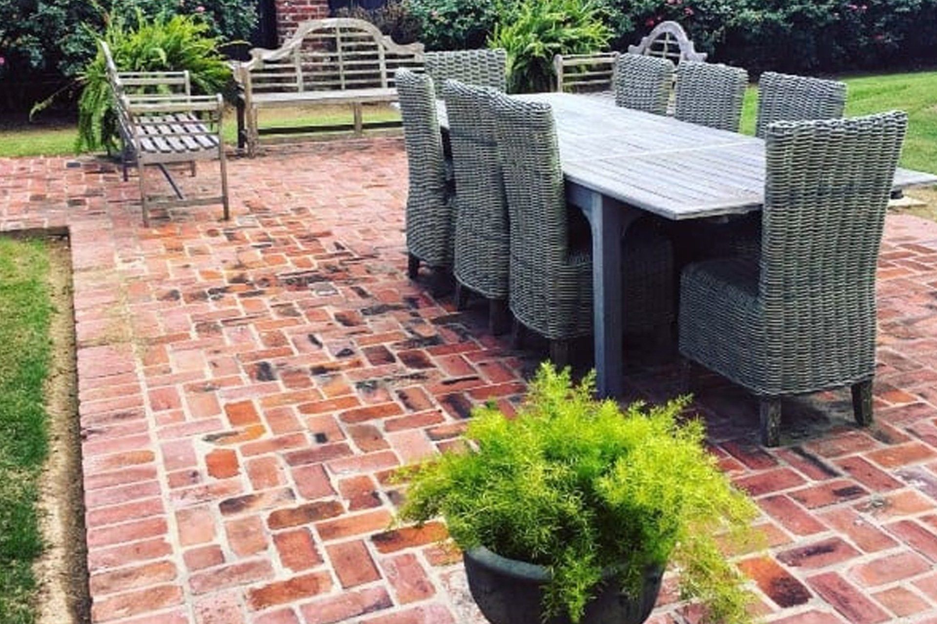 Brick patio with a large table and chairs; bench and potted plant in the background.
