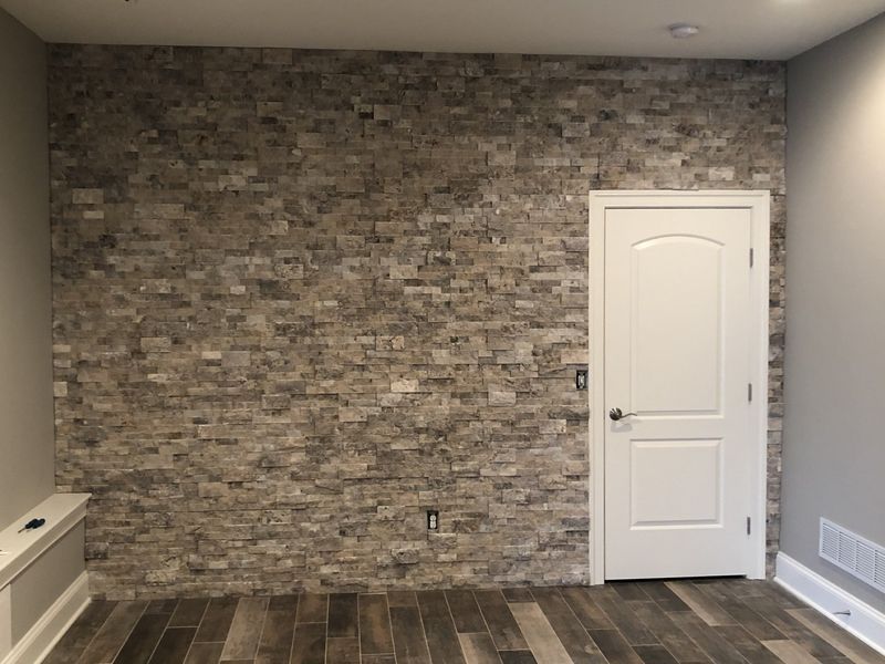 Stone accent wall with white door, wood flooring, and beige walls.