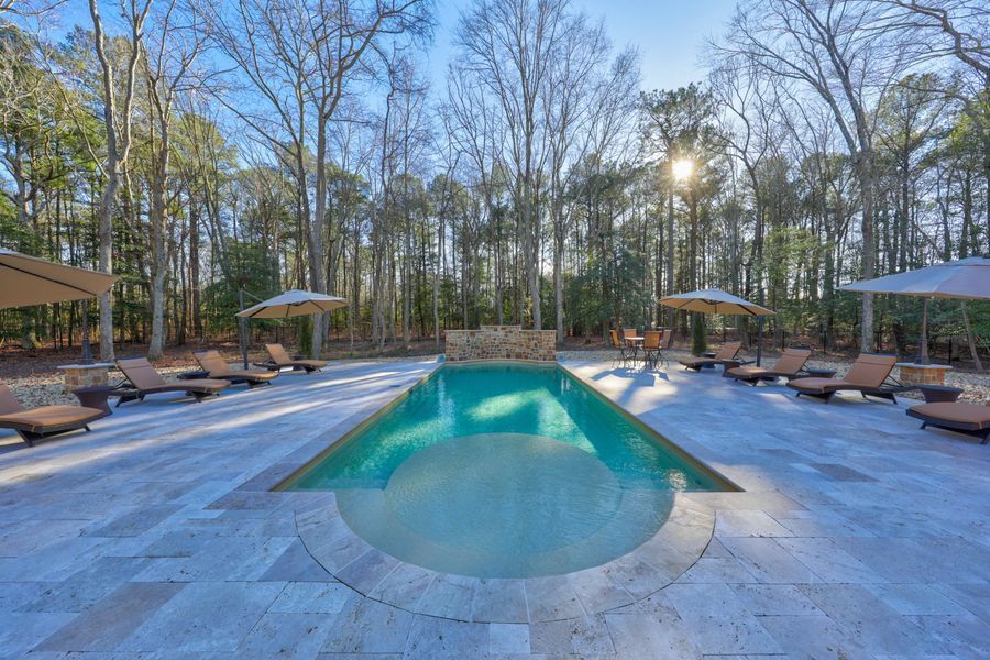 Swimming pool surrounded by lounge chairs and trees on a sunny day.