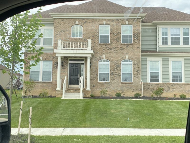 Two-story house with brick and green siding, white trim, and a small front balcony. Green lawn in front.
