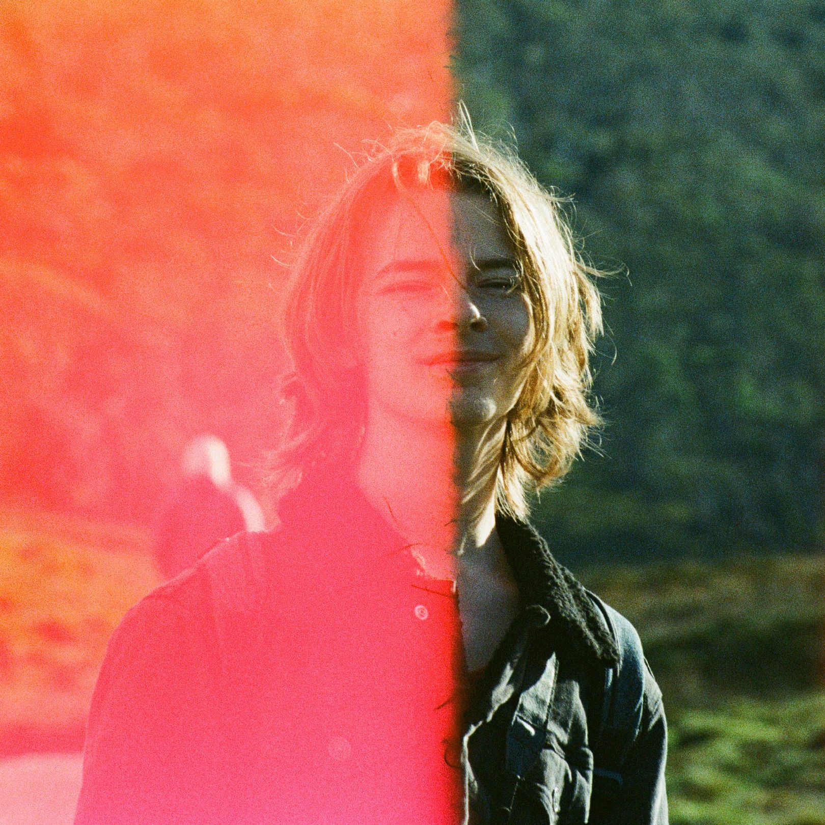 A person with shoulder-length blonde hair split down the middle by red light. They are wearing a denim jacket.