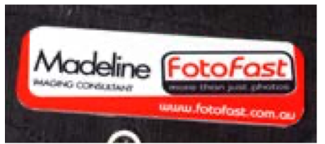 Silver keychain with a woman's photo in a subway station, smiling, leaning on her arm, red scarf, blue sweater.