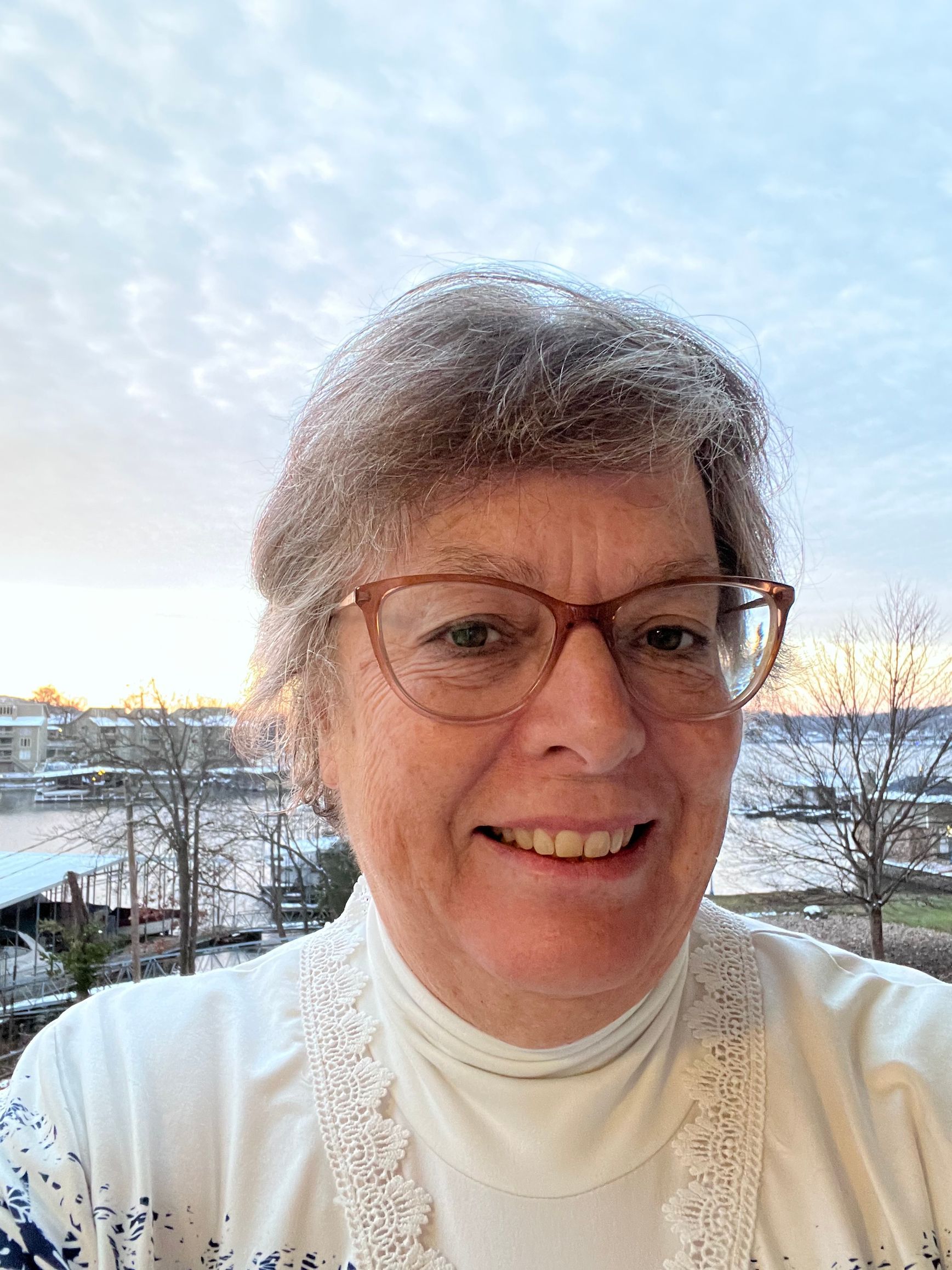 Woman with glasses smiling, next to a man, in front of a red rock formation.