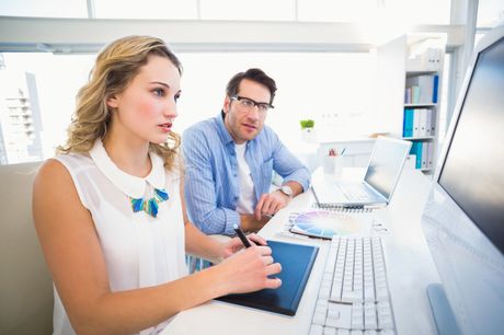 a man and a woman sitting at a desk looking at a computer screen