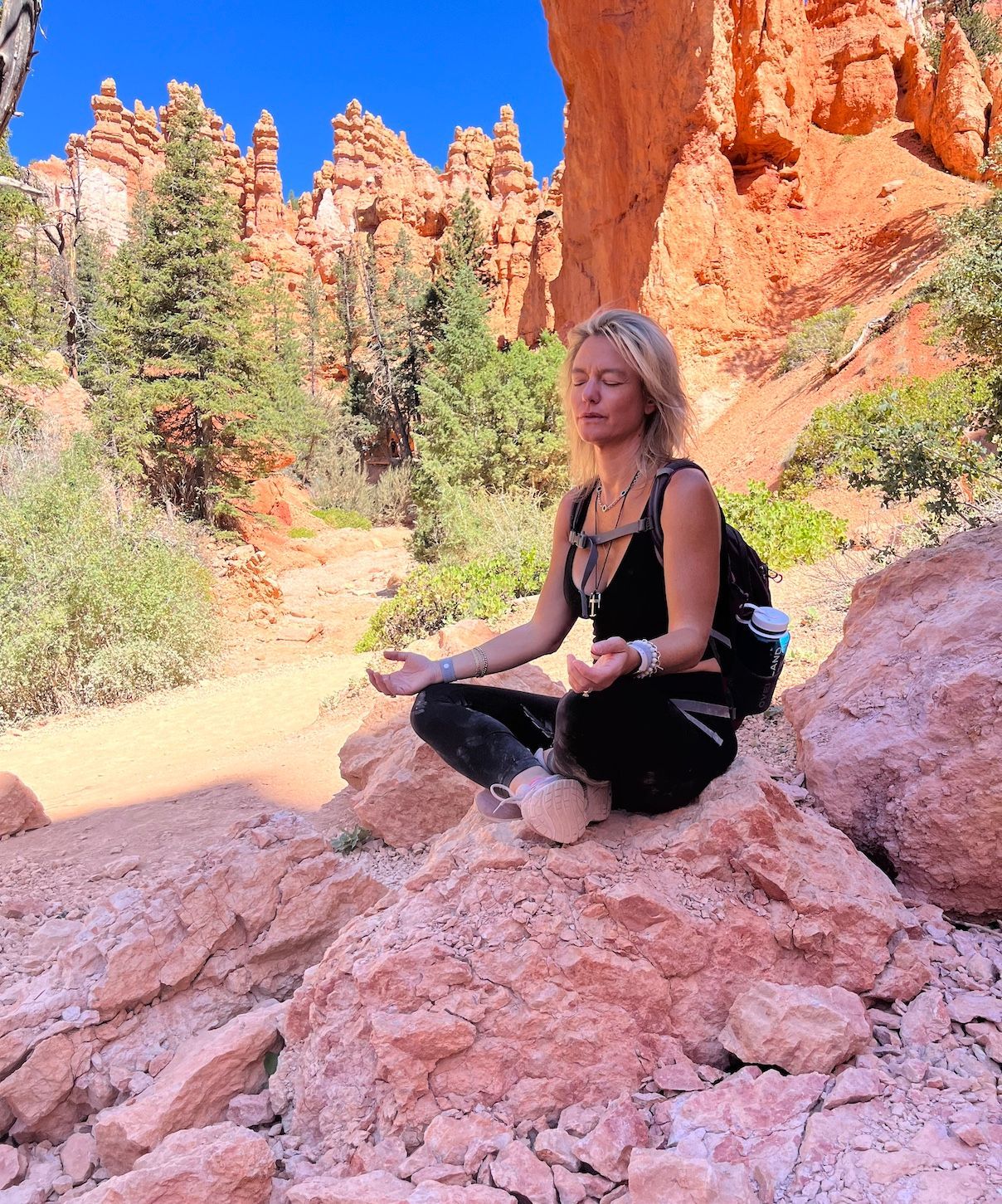Woman with blonde hair, smiling, in blue button-up shirt and jeans, hands in pockets.