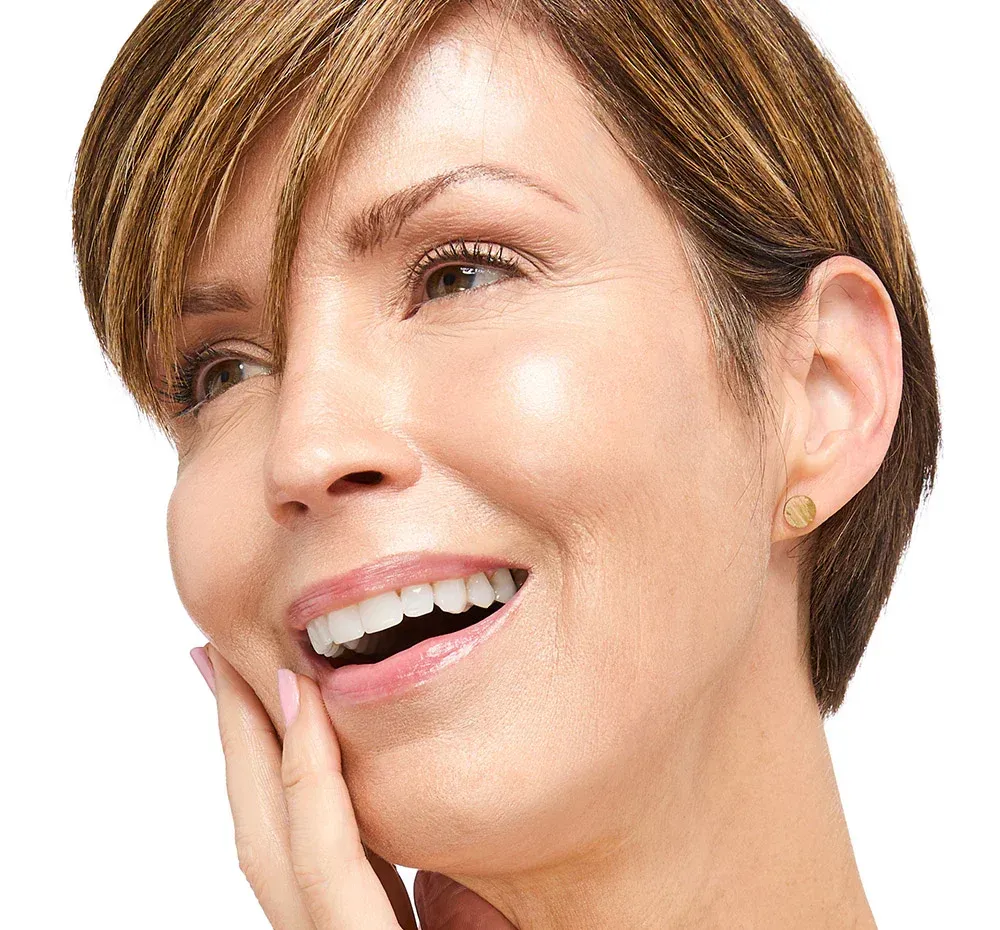 Woman with short brown hair smiles, touching her face.