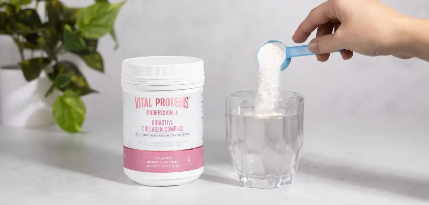 A person is pouring protein powder into a glass of water.