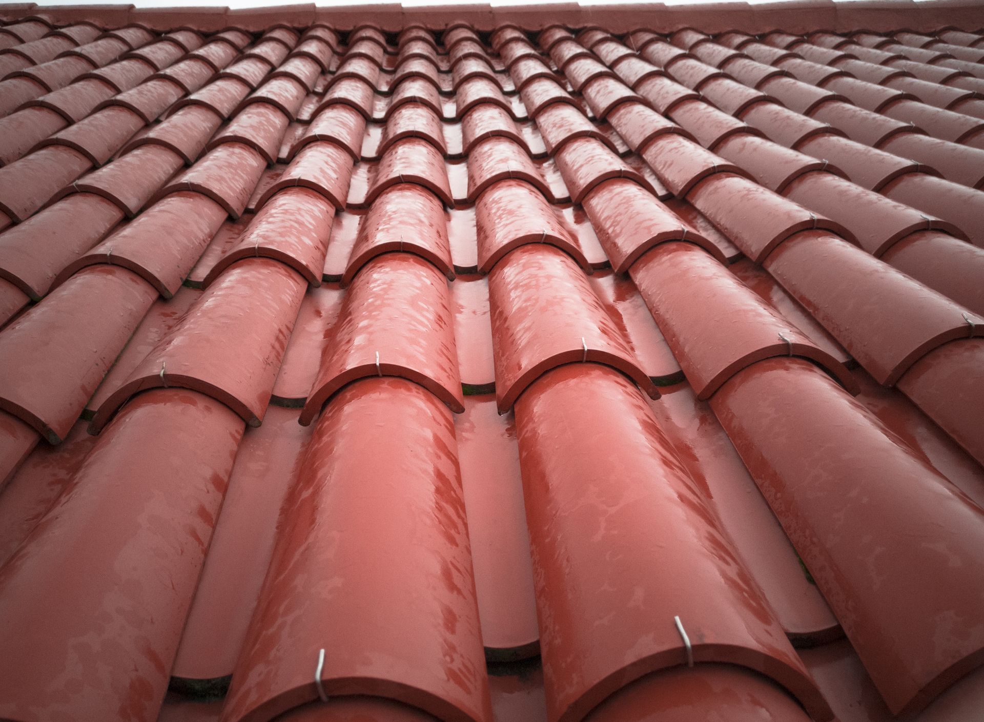 Red clay tile roof, close-up view, angled from below, showing rows of overlapping tiles.