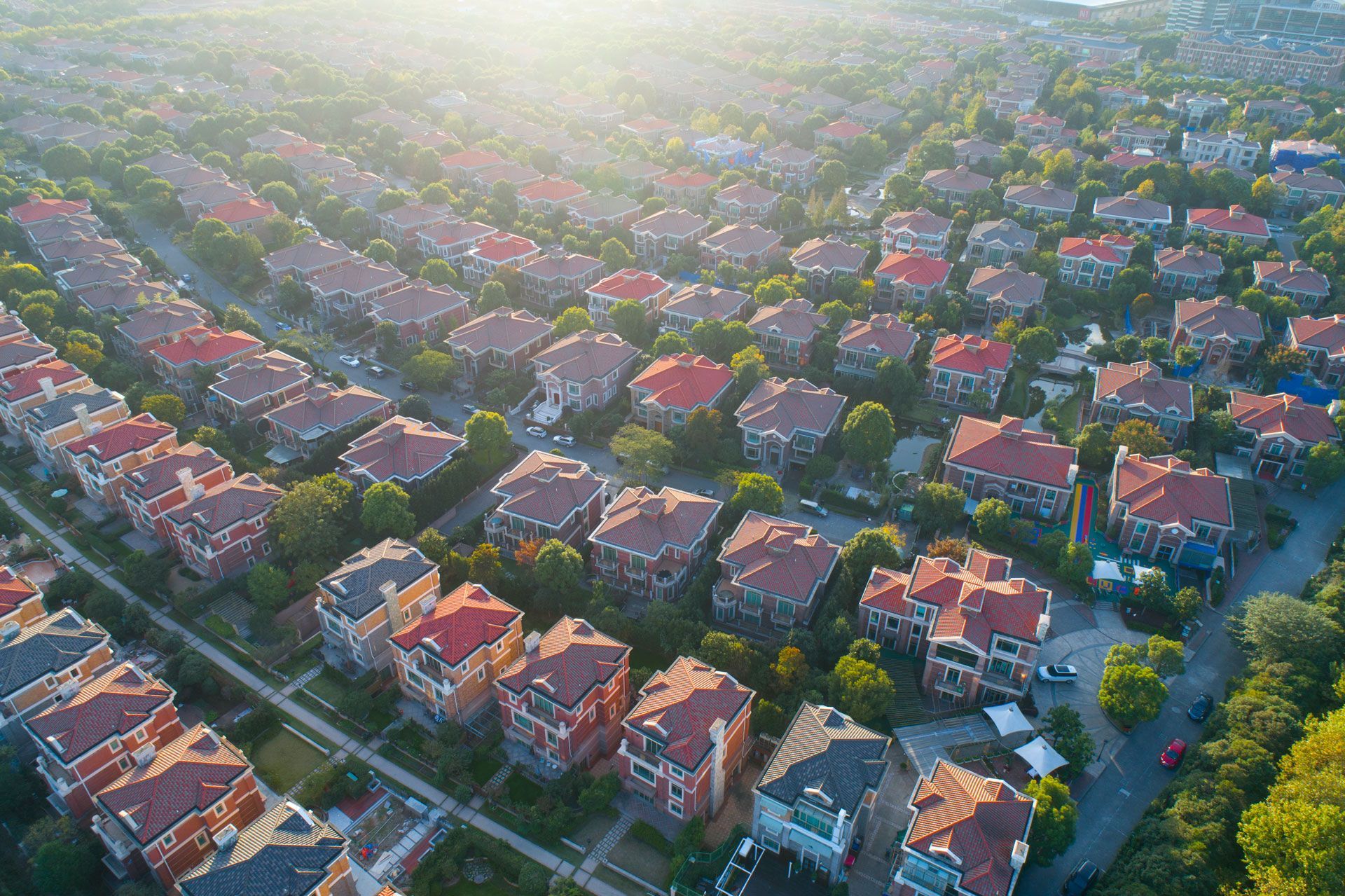 Aerial view of a suburban neighborhood with rows of houses with red-tiled roofs and green trees. Aerial view of a suburban neighborhood with rows of houses with red-tiled roofs and green trees.