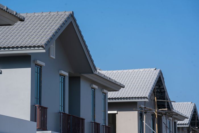 Row of light grey houses with matching tiled roofs against a clear blue sky.