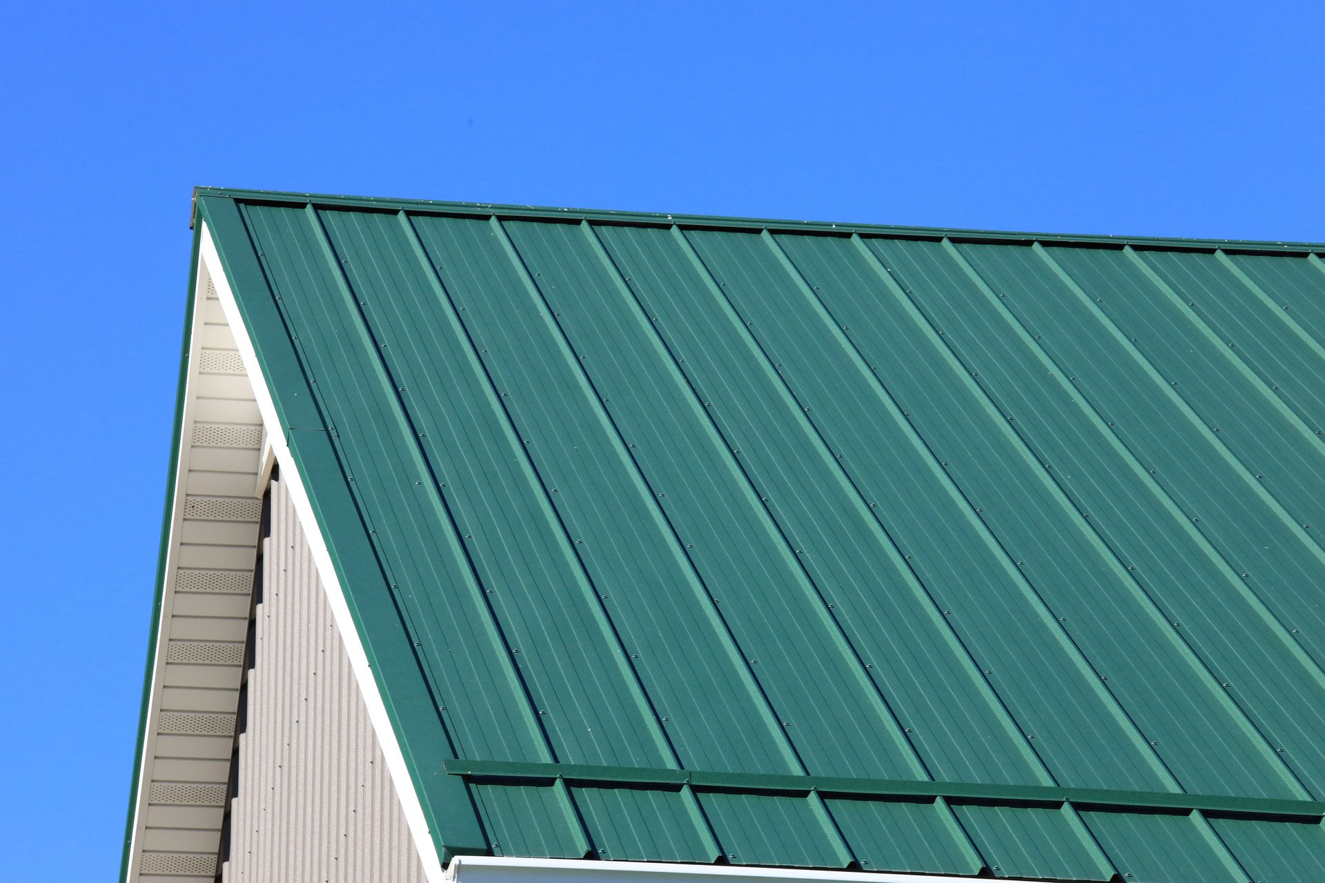 Green metal roof against a clear blue sky. Corner of a building with white trim visible.