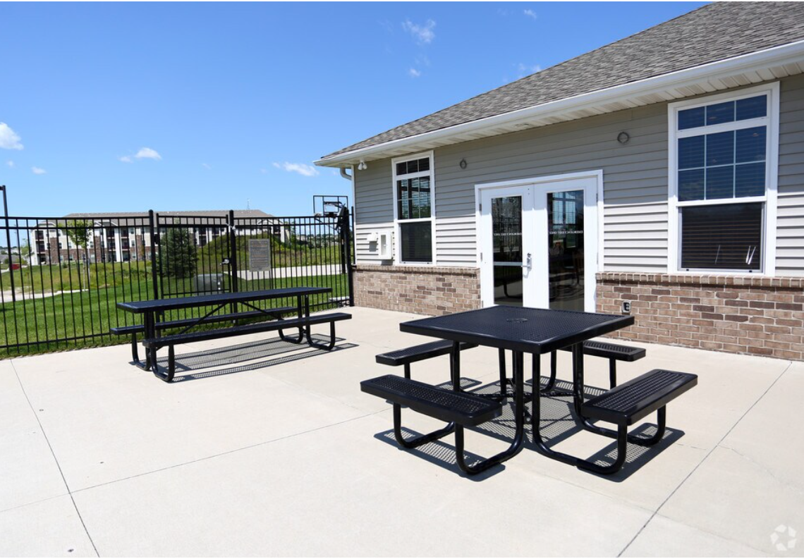 Outdoor patio with black picnic tables; a building with windows and doors in the background.