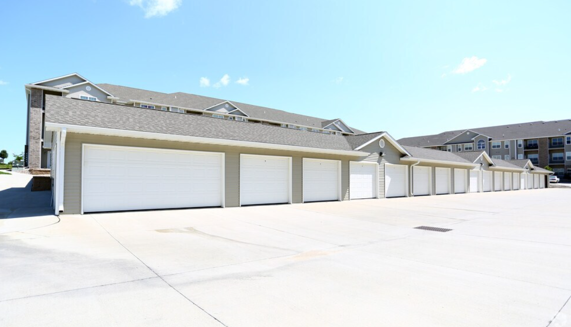 Row of white garage doors in front of a beige building under a blue sky.