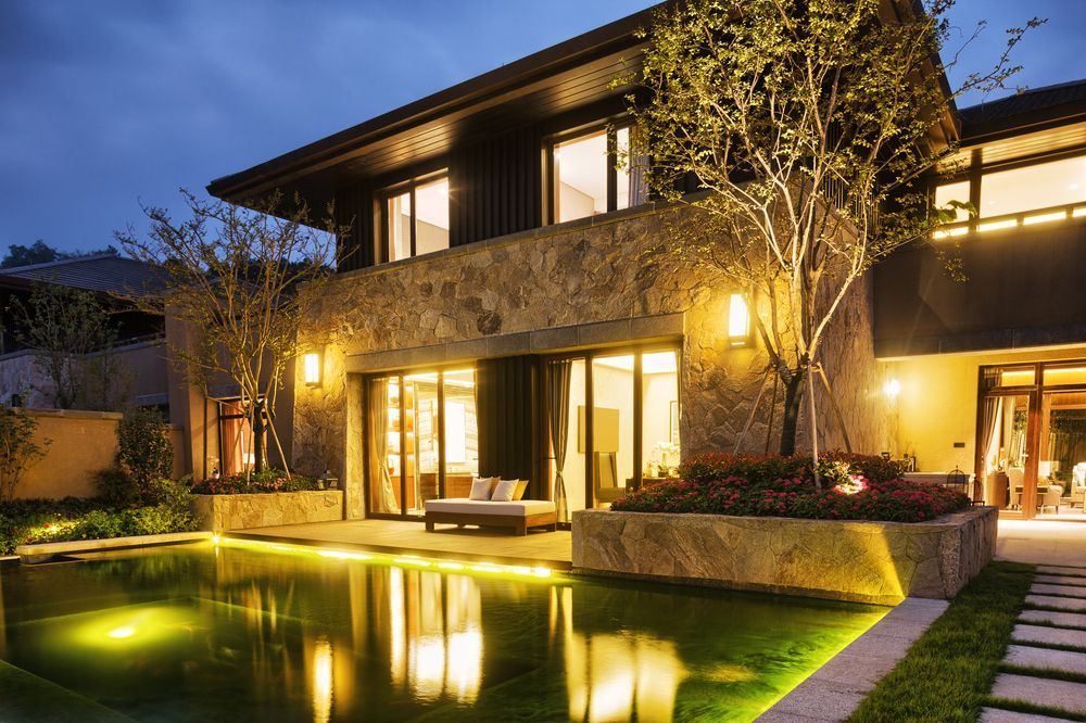 A large house with a swimming pool in front of it at night.