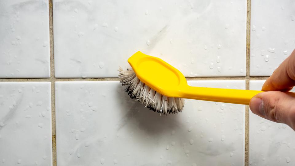 A yellow brush being used to clean grout lines between tiles, removing dirt and stains effectively.