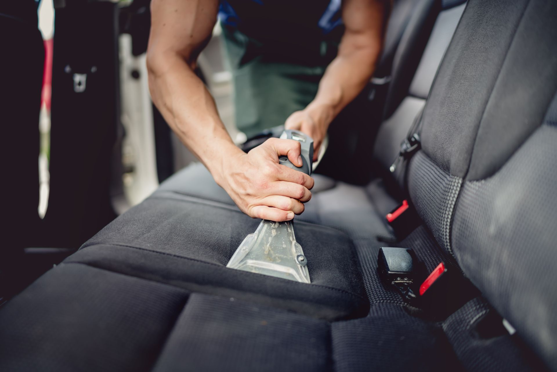 Person using a handheld vacuum cleaner to clean the interior of a car, removing dirt and debris from the seats.