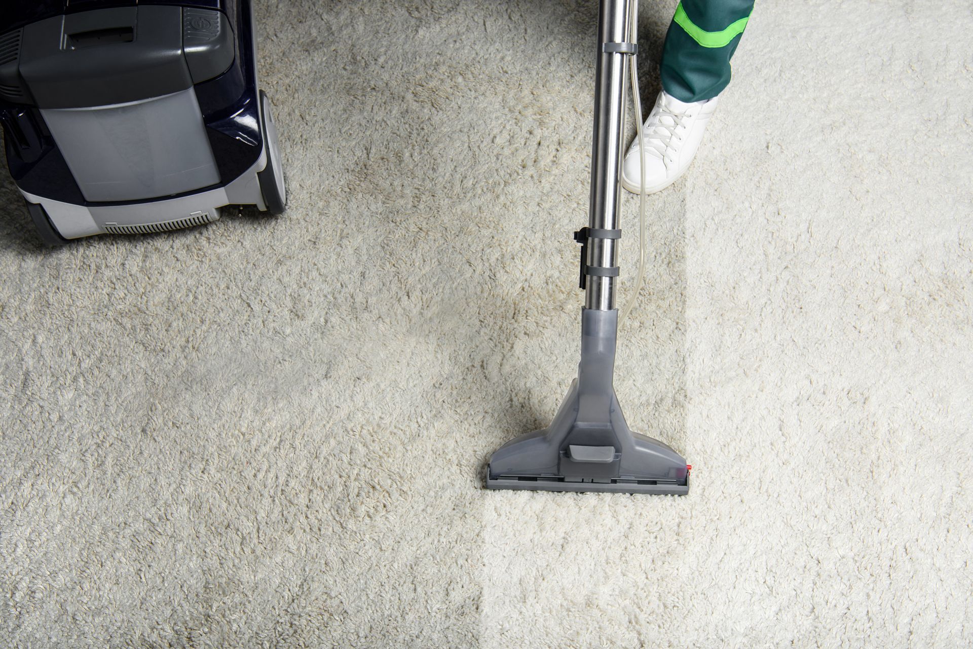 Person professionally cleaning a white carpet with a high-angle view using a powerful vacuum cleaner, ensuring thorough cleanliness and removing debris effectively.