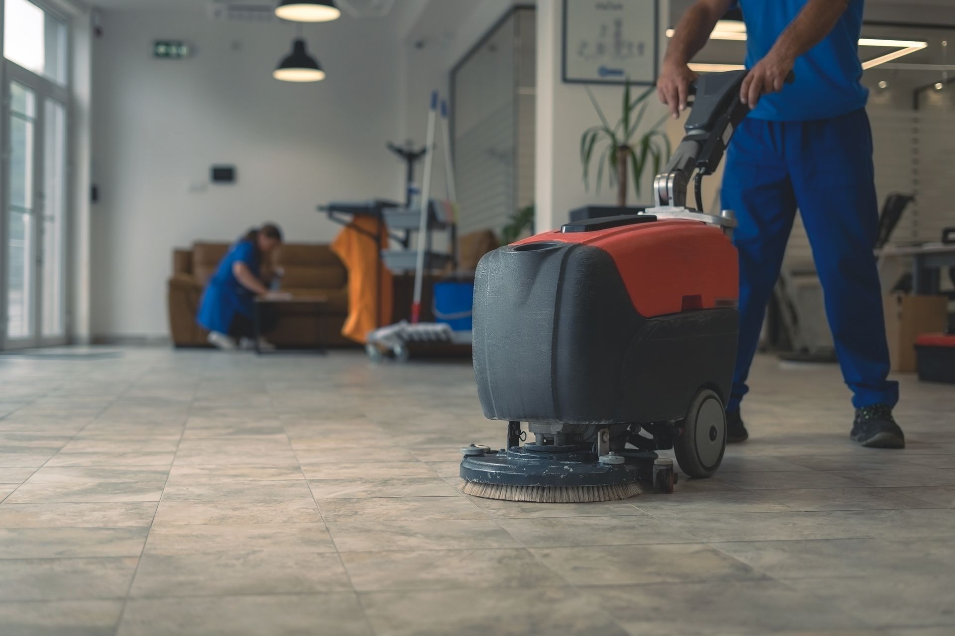 A scrubber machine efficiently cleans a hard floor, while another cleaner works diligently in the background.