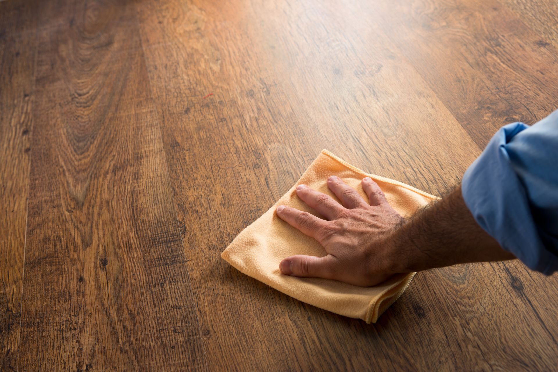 A person performing hardwood maintenance by gently polishing the floor using a soft cloth.