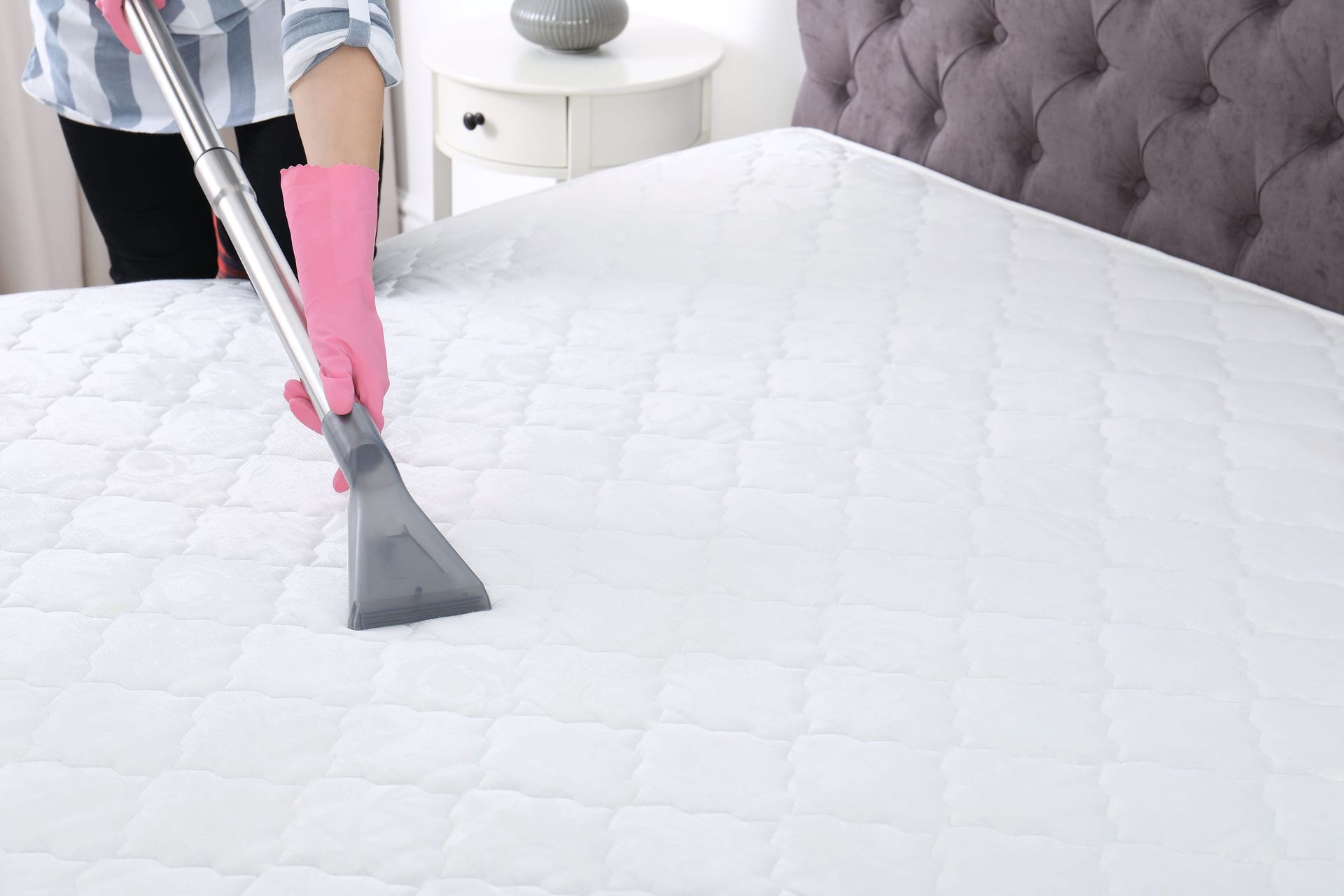A person using a handheld vacuum cleaner to clean a mattress surface.