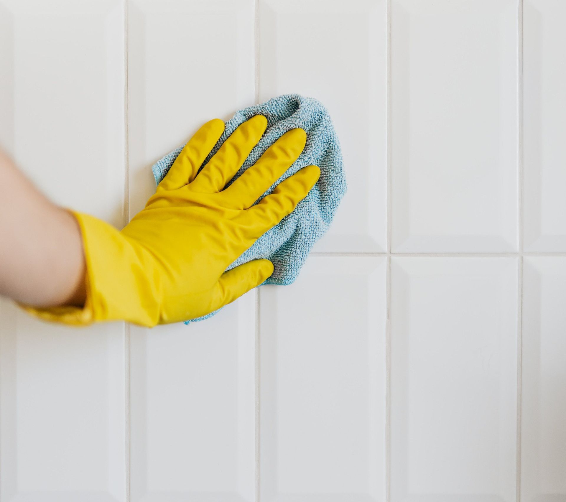Cleaner wiping a cloth along grout lines between tiles to remove dirt and stains, revealing a cleaner and brighter surface.