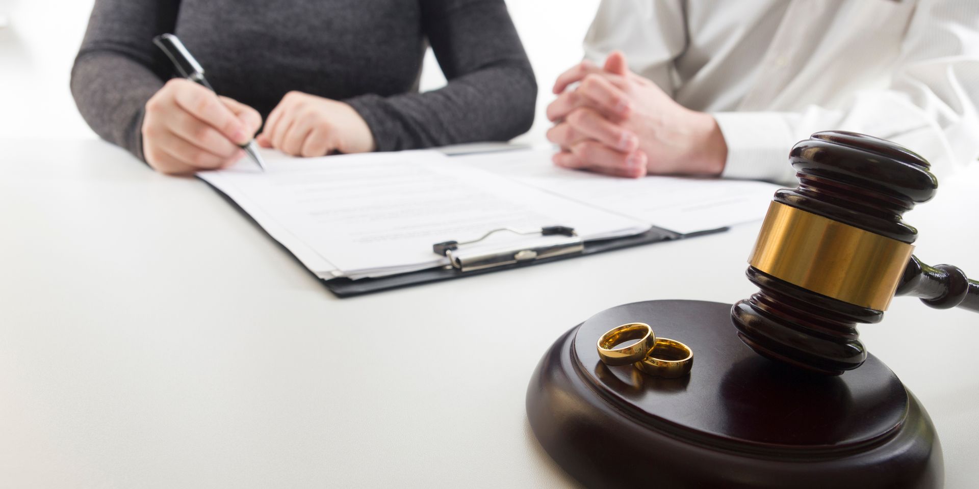 A couple is sitting at a table with a judge 's gavel and wedding rings.