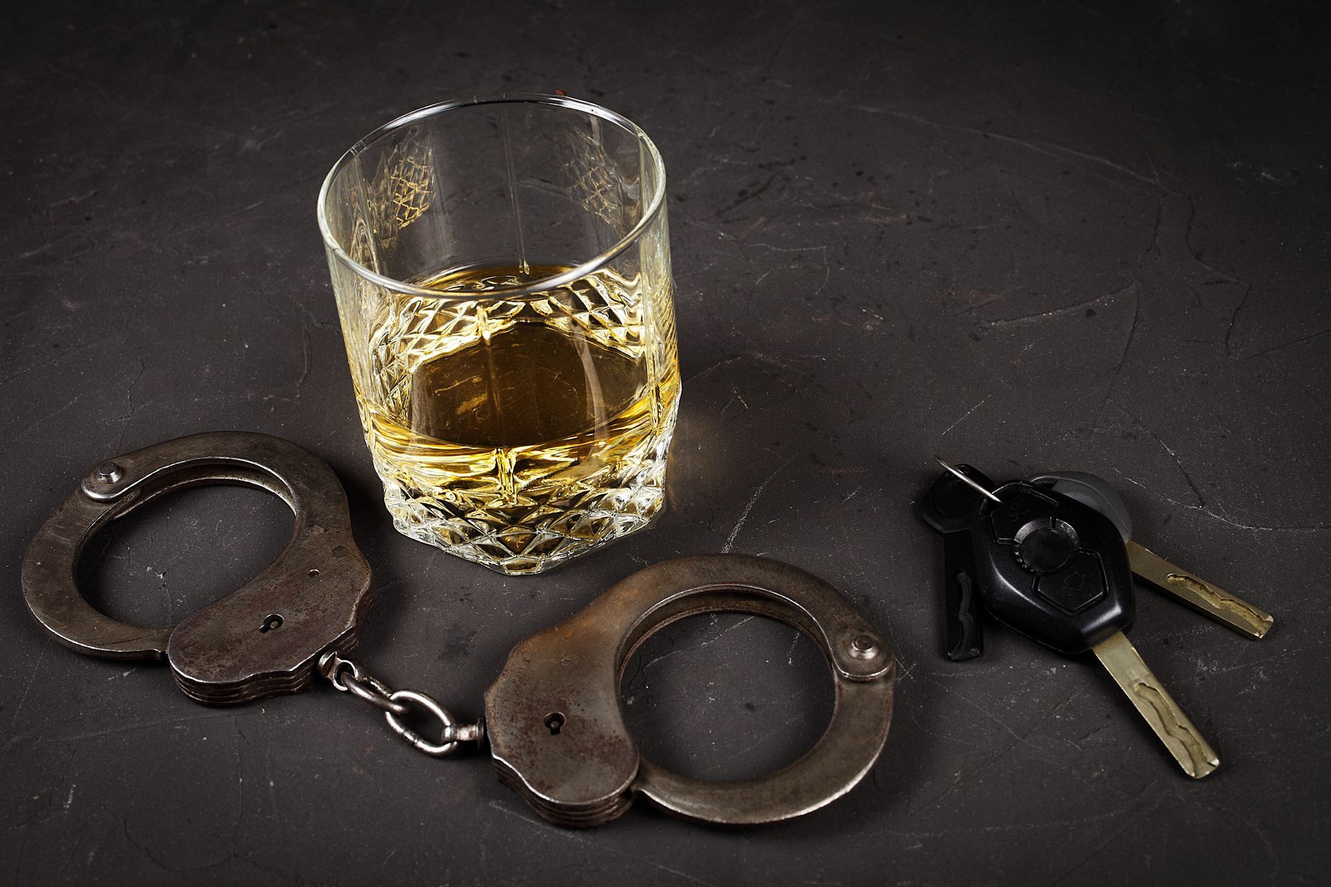 A glass of whiskey , handcuffs and car keys on a table.