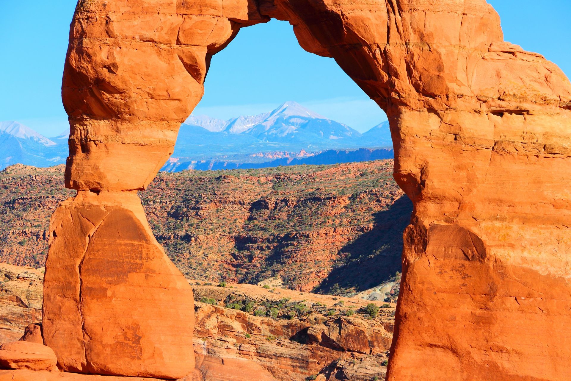 A rock arch in the desert with mountains in the background