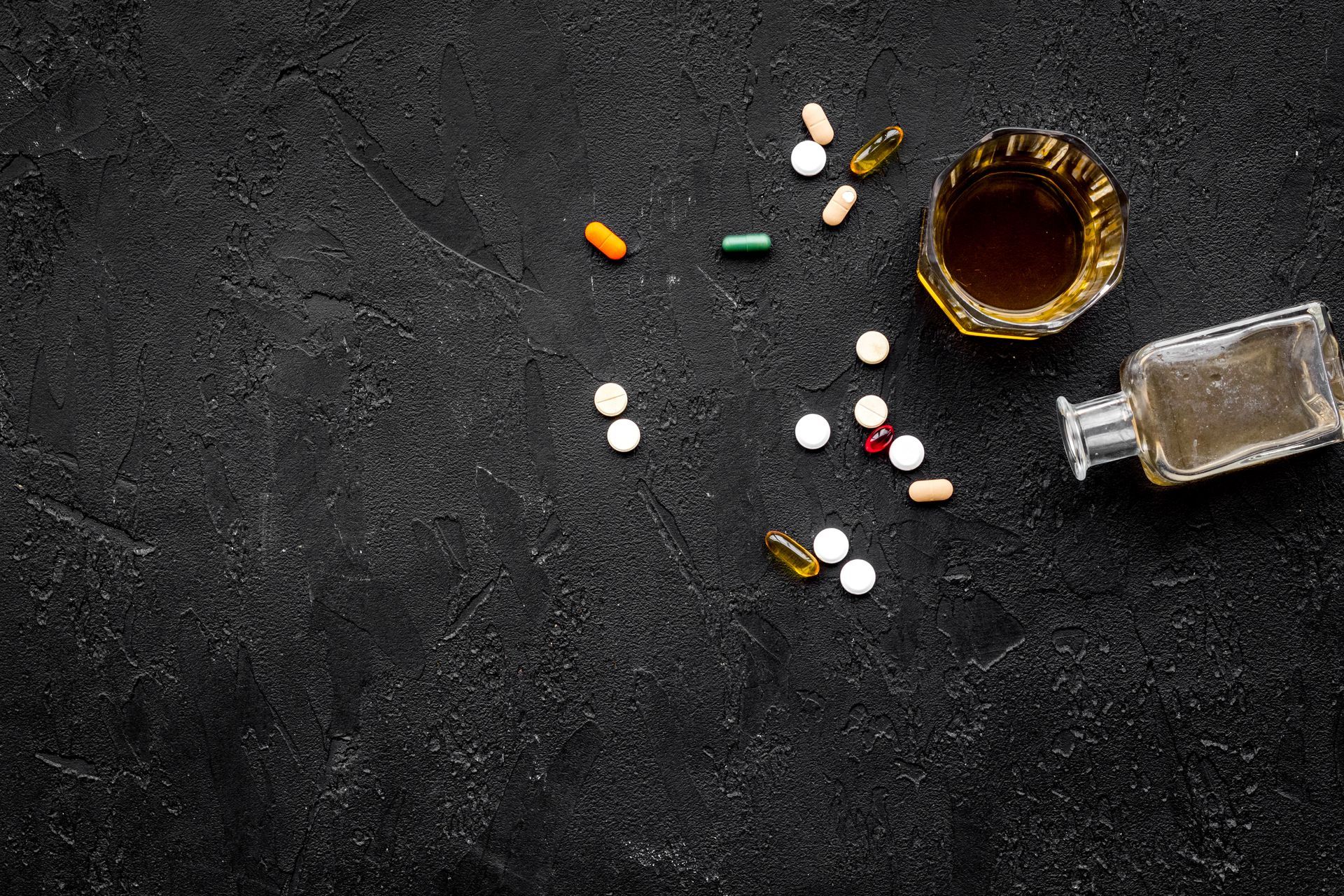 A bottle of alcohol , pills and capsules on a black background.